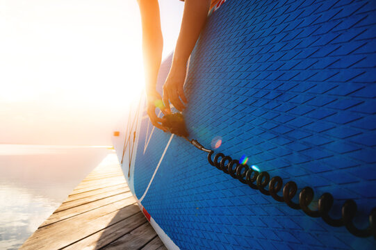Female hands of young Caucasian woman fastening leash on paddle board at sunset