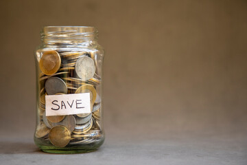 A glass jar labeled 'SAVE' is brimming with coins, signifying budgeting, frugality, and responsible...