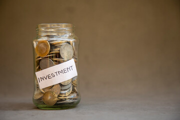 A glass jar filled with coins labeled investment symbolizes savings, security, finance, and future financial planning, representing popular methods of wealth growth and budget management.