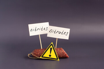 A fragment of smoked sausage and warning labels nitrates and nitrites in close-up on a dark...