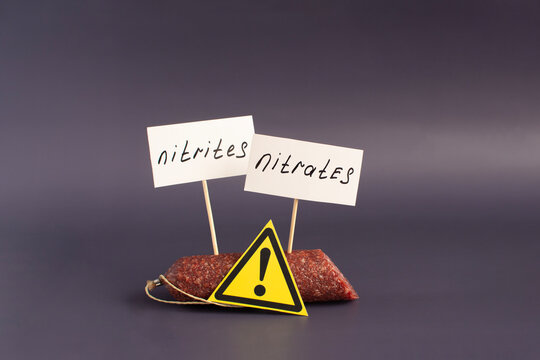 A fragment of smoked sausage and warning labels nitrates and nitrites in close-up on a dark background