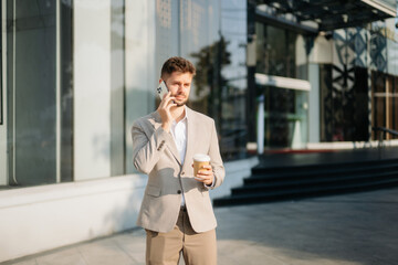 Fototapeta premium Handsome unshaven businessman walking with laptop, tablet and smartphone on city