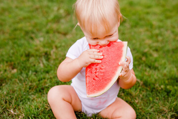 Messy baby eating juicy watermelon with stained shirt on summer day