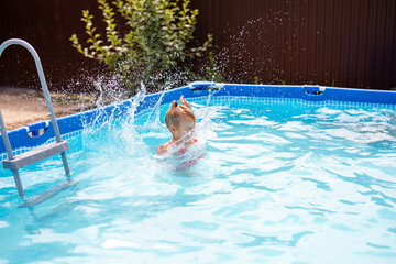 Child making a big splash in a backyard pool on a sunny day, caught in motion