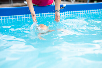 Baby boy learning to swim in a backyard pool with adult support on a warm sunny day