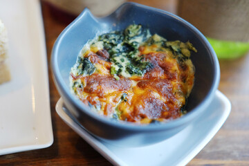 Baked Spinach with cheese in blue ceramic bowl on wooden table