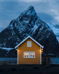 Winter auf den Lofoten in Norwegen mit traditionell gelbem Rorbua in Sakrisoy am verschneiten Fjord...