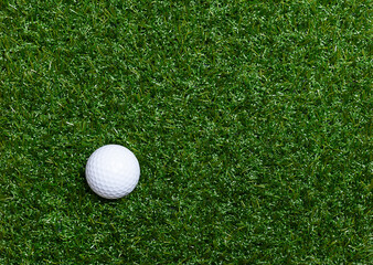 Golf ball on artificial turf. Single, white American golf ball with special notches, on the bottom left side of a flat plastic grass surface, from above, with empty space for text or other purposes.