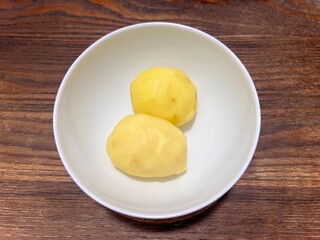 Horizontal photo of peeled potatoes, placed in a white ceramic bowl on a wooden table