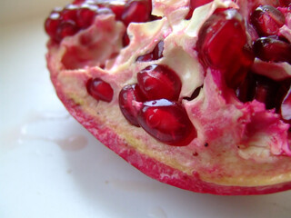 Close-up of a ripe pomegranate cut open to reveal juicy red seeds and textured interior against a...