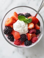 Close-up of a dessert in a glass bowl. the bowl is filled with a variety of fresh berries, including strawberries, blackberries, raspberries, and blackberries.