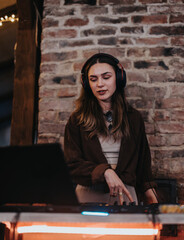 A young woman wearing headphones as she DJs music in a stylish bar. The exposed brick background...