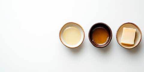 Three ceramic bowls with cooking fats: melted lard, ghee and a block of solid animal fat on white background