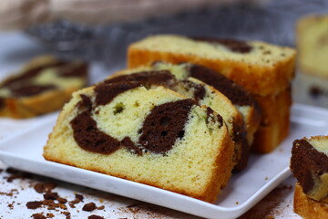 Slices of moist marble cake with chocolate and vanilla swirls, placed on a white surface.