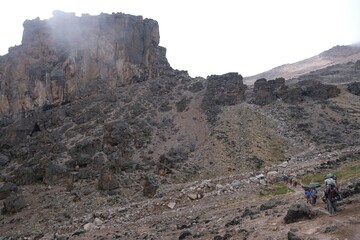Kilimanjaro, Tanzania: Misty scenery of Lava Tower and silhouettes of trekking people. Machame Route, trail from Shira Camp to Barranco Camp. © Iwona