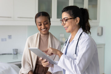 Happy senior Caucasian doctor and young African patient women watching medical examination...