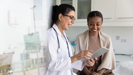 Happy senior practitioner woman and cheerful young African patient woman watching examination...