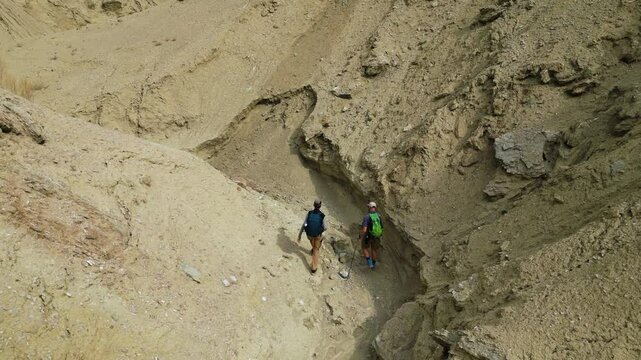 Male travelers walking through a canyon among sandy sedimentary rock cliffs. Altyn Emel National Park. Kazakhstan