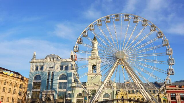 Kyiv, Ukraine - March 28, 2025: Ferris wheel at Kontraktova Square in Podil, Kyiv, with historic buildings and a clear blue sky in the background, showcasing urban life.