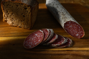 Slices of cured salami beside hearty bread on a wooden cutting board