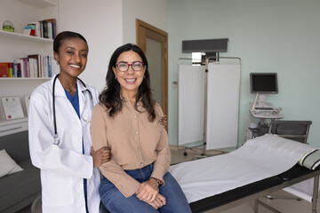 Positive empathetic caring young African doctor woman touching shoulders of happy healthy mature...
