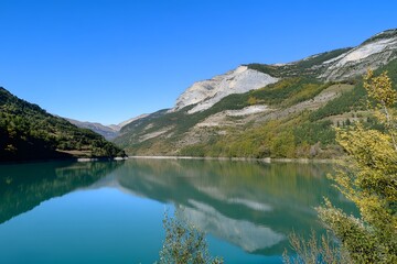 Naklejka premium Lake reflects mountains and trees under a clear blue sky, serene view