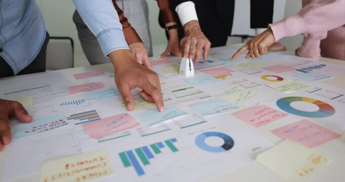 Diverse businesspeople analyzing report shown in pie charts and graphs, discuss paperwork, making analysis of stats data during group meeting in boardroom, close up. Researching, brainstorm, teamwork