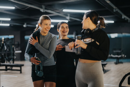 Three women share a friendly conversation in a modern gym environment after finishing their workout session, depicting camaraderie and active lifestyles.
