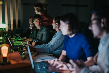 A group of business coworkers engage in a collaborative meeting. The team is focused and working late at night using laptops, fostering teamwork and productivity in a modern office environment.