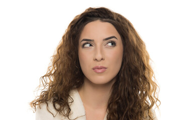 Woman with curly brown hair in white bathrobe looking upward with contemplative expression against...