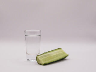A glass of vodka and half a green cucumber, on a light background, front view, close-up