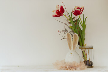 Easter bunny figurine with a nest of feathers and tulips on a white background. Easter decoration...