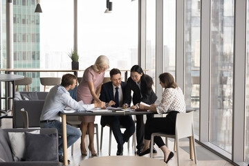 Fototapeta premium Group of five businesspeople engaged in business meeting in modern office, focusing on documents around table, discussing business strategy, make financial decision, analyzing or reviewing information
