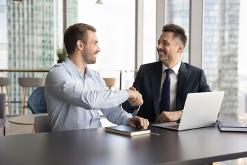 Two businessmen shake hands in modern skyscraper office, gesture symbolize closing deal, make...