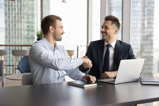 Two businessmen shake hands in modern skyscraper office, gesture symbolize closing deal, make agreement, conclude partnership, express mutual respect, thanking for professionalism finish consultation