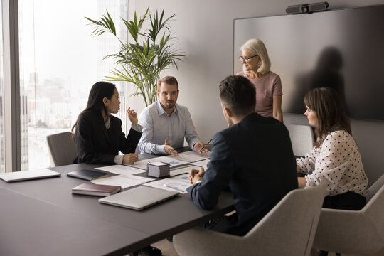 Millennial businessman addressing group of professionals seated together at table, makes speech looks confident, holds position of authority or leadership in formal meeting, negotiate with shareholder