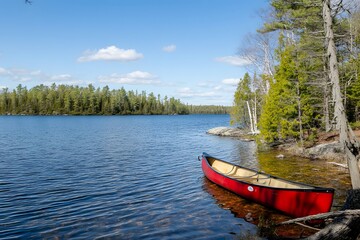 Red canoe rests beside a calm lake with lush forest backdrop