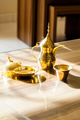 Golden Arabian Coffee Set in Sunlit Elegance: Dallah Pot and Cups on a Gleaming Table, A Study in Cultural Tradition and Warm Light in a Refined Setting