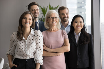 Obraz premium Group of five older and younger satisfied and successful male female colleagues standing together, smiling, looking aside, exude self-assurance and professionalism. Diversity in workplace, teamwork