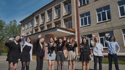 Happy high school students happily waving goodbye on their last sunny school day in front of their school