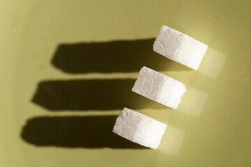 Three Cubes of Sweet: White Sugar Cubes Cast Elongated Shadows on a Muted Green, A Minimalist Study...