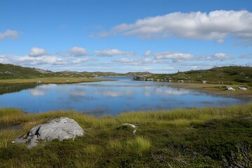 Serene lake reflects sky, amidst grassy land under a blue sky