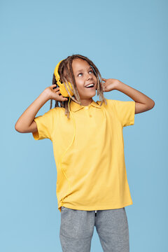 Trendy little boy with african dreads listening music in headphones dancing over blue background