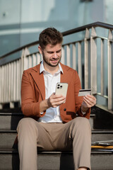 Male businessman use credit cards to conduct financial transactions through phones.