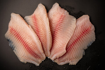 Fresh tilapia fillet on black background, top view.