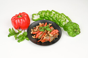 Colorful Fresh Vegetable Dish with Red and Green Bell Peppers, Chopped Walnuts, MakdouS and sliced Tomatoes, with Mint on a Black Plate, Surrounded by Fresh Ingredients on a White Background

