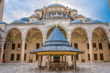 Fototapeta premium Majestic view of the inner courtyard and ablution fountain of the Nuruosmaniye Mosque in Istanbul showcasing Ottoman architecture with domes, arches, and intricate designs under a cloudy blue sky
