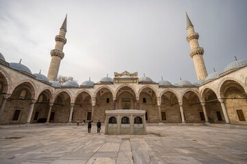 Majestic view of the inner courtyard of the Süleymaniye Mosque in Istanbul showcasing its grand arches, domes, and towering minarets under a serene sky with a few visitors admiring the architecture