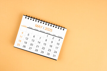 Top view of May 2025 desk calendar on yellow pastel background.