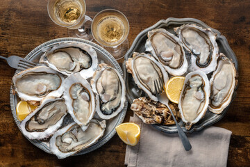 Fresh raw oysters on ice, overhead flat lay shot of two platters with champagne and lemon slices, on a rustic wooden table